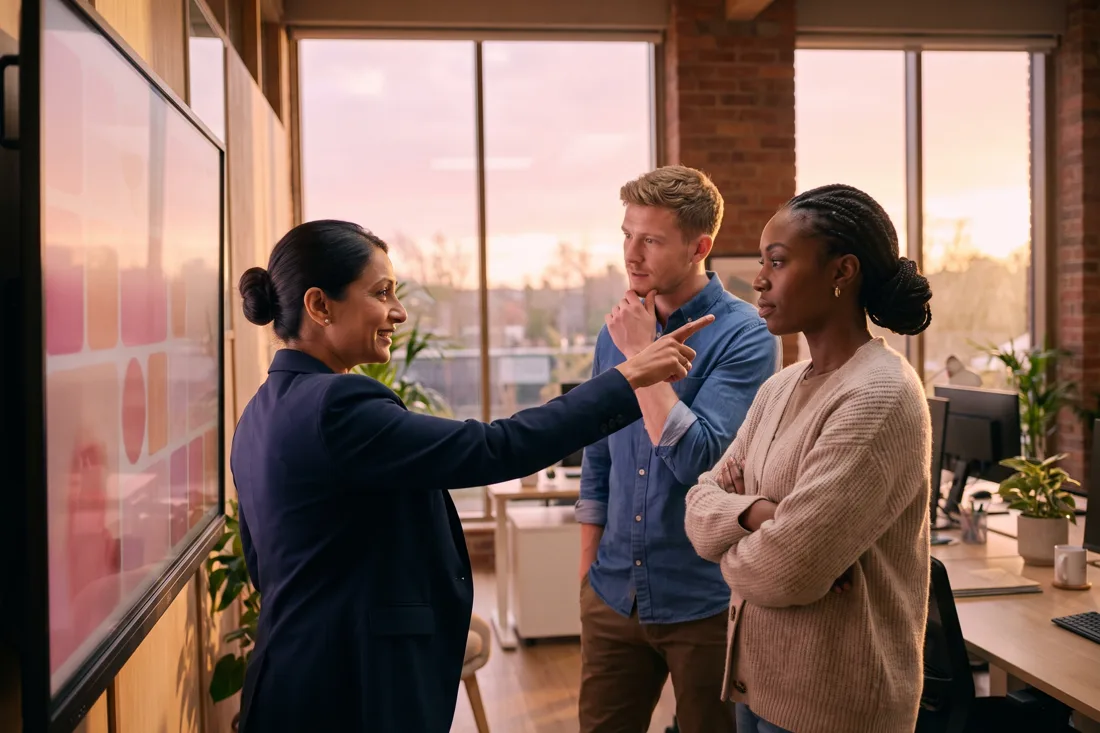 Three estate agency colleagues around a wall-mounted screen showing branch listings in a modern regional office