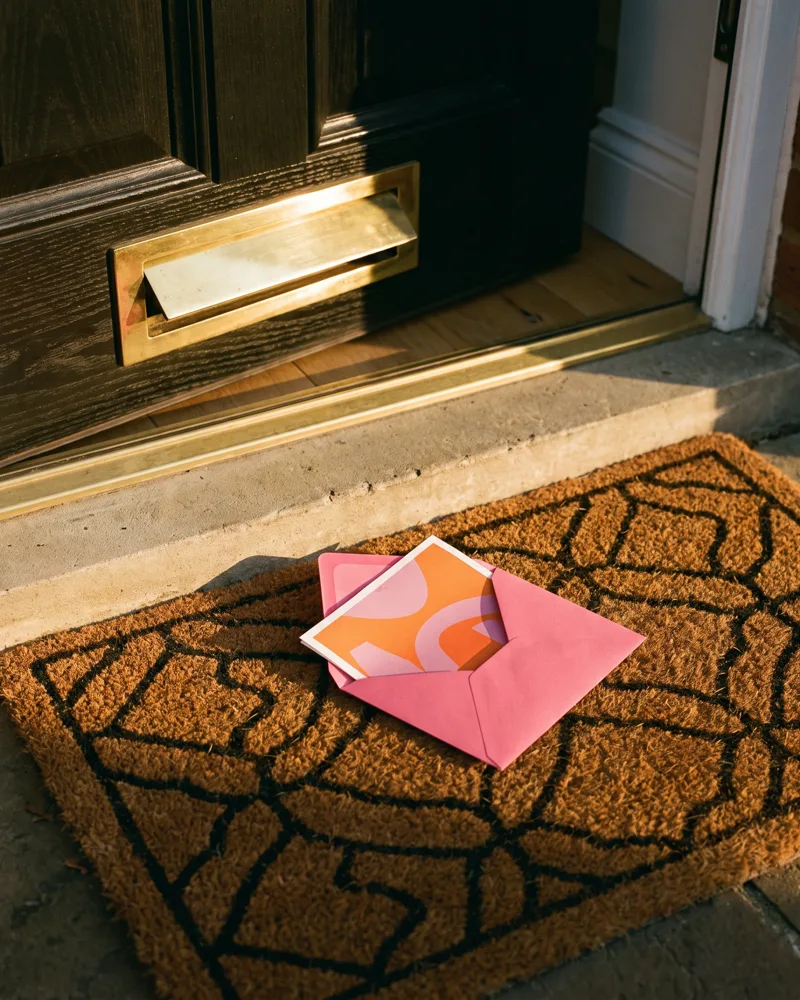 A designed letter falling through a brass letterbox onto a doormat in a British hallway
