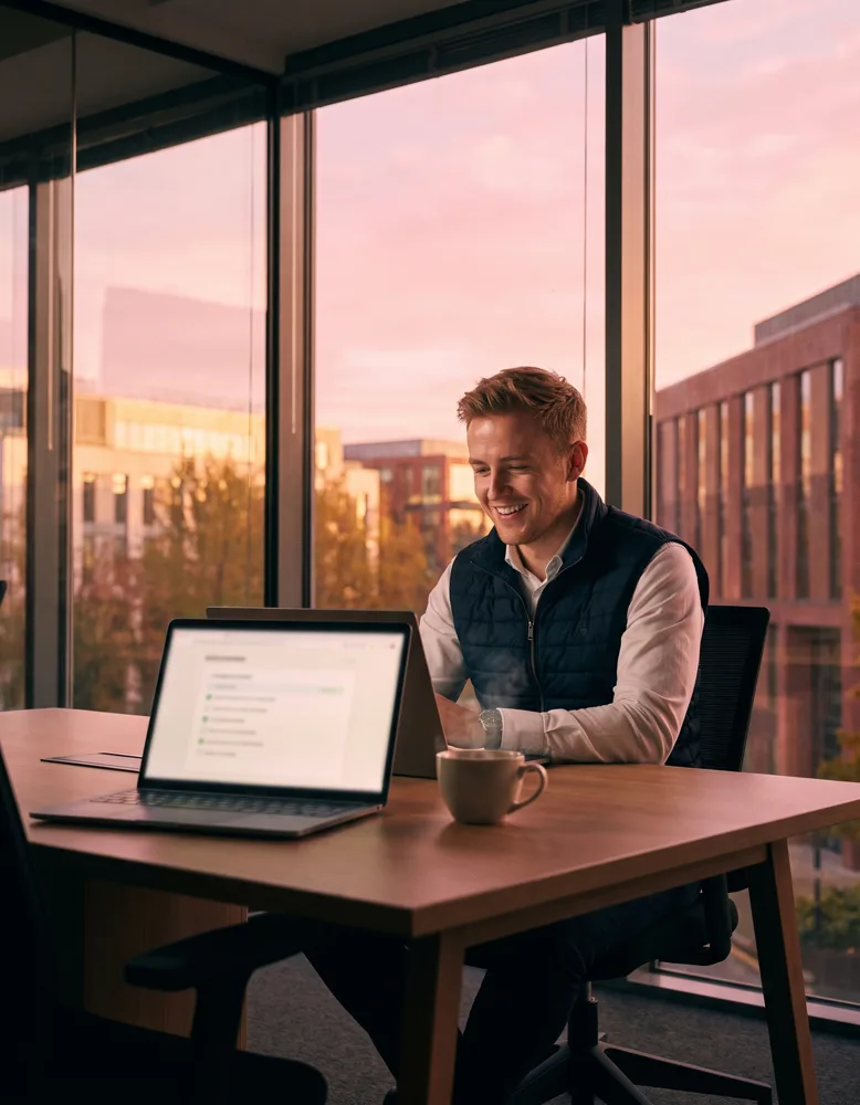 An estate agent at a modern desk in a glass-fronted office the next morning, coffee beside an open laptop showing a completed checklist