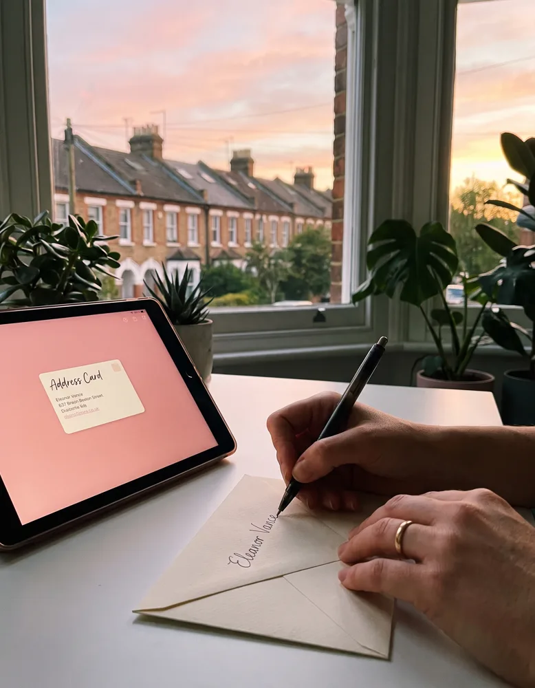 A close view of hands holding a smartphone showing a glowing rose-pink address card mid-reveal, a British street visible through the window behind