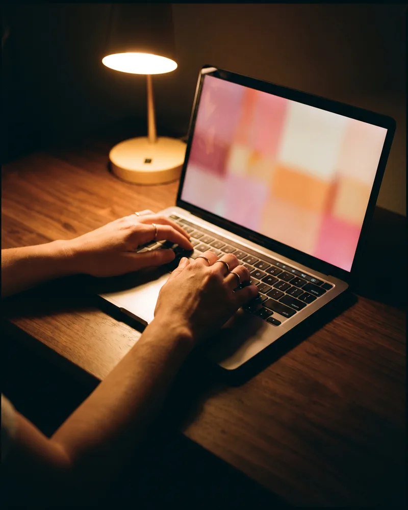 An estate agent's hands on a laptop keyboard, the screen showing a social post assembling from a listing photo and colourful brand panels